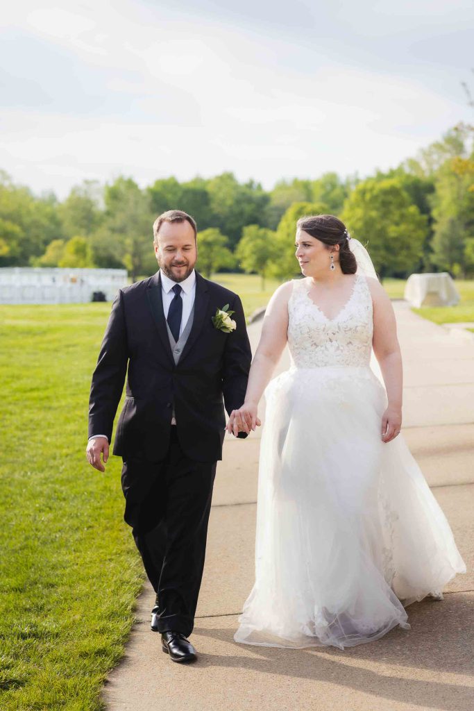 A wedding portrait of a bride and groom walking down a path in a park.