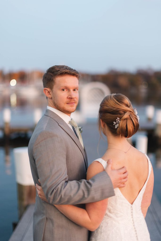 A wedding portrait of a bride and groom on a dock at dusk.