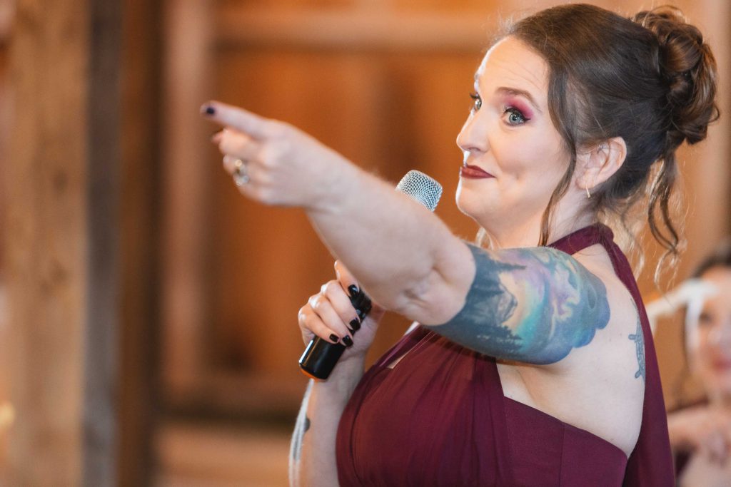A woman with tattoos at a wedding reception posing near a microphone.