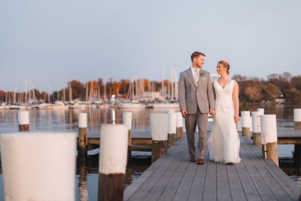 A wedding portrait of a bride and groom standing on a dock at a marina.
