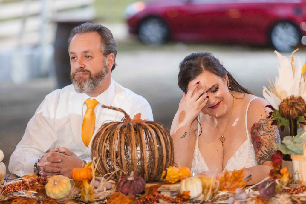 A bride and groom celebrating their wedding at a reception table adorned with pumpkins.