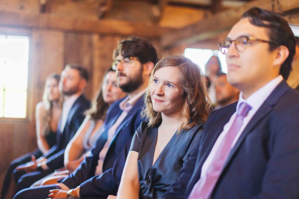 A group of people sitting in a row during a wedding ceremony in a barn.