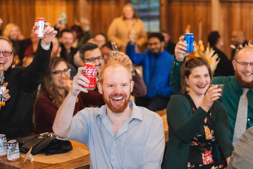 A group of people holding up cans of coca cola at a wedding reception.