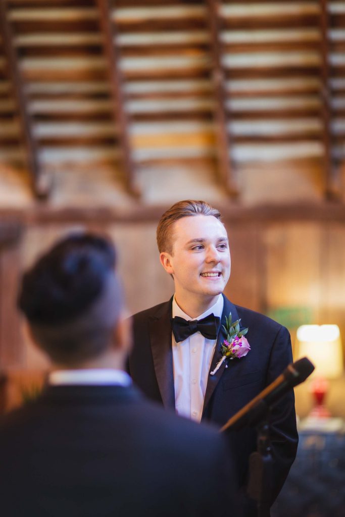 A groom smiles at the bride during their wedding ceremony.