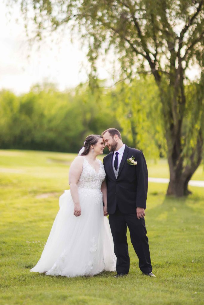 A portrait of a wedding couple kissing in front of a tree.