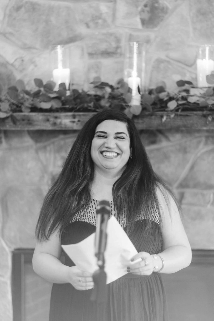 A woman smiles as she reads a speech at a wedding ceremony.