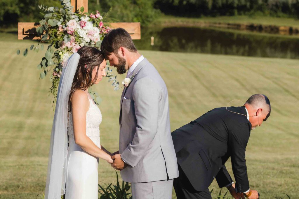 A wedding ceremony with a bride and groom standing next to a cross in a field.