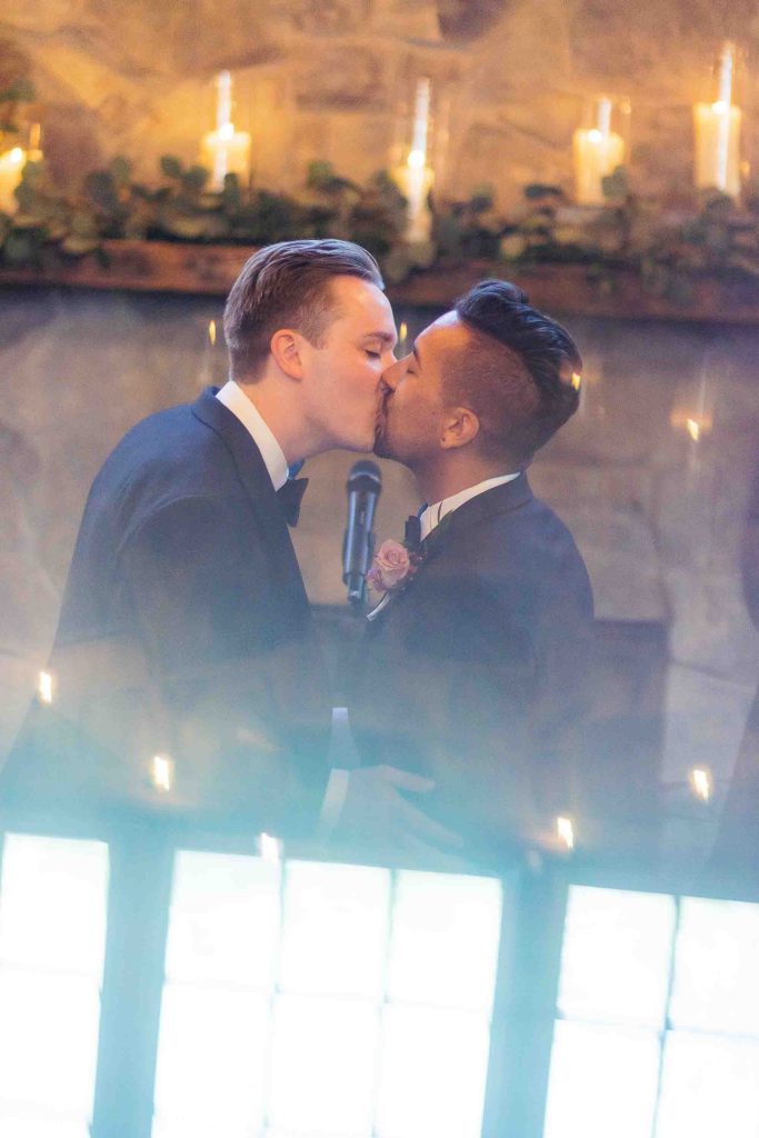Two men sharing a wedding kiss in front of a mirror.