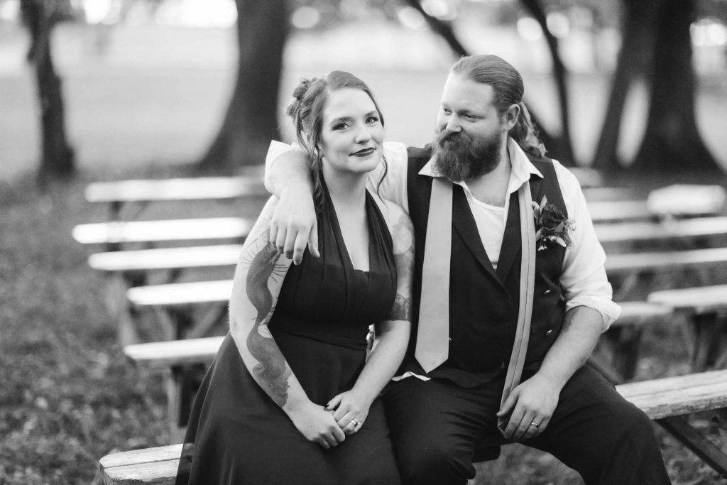 A black and white wedding portrait of a couple sitting on a bench.
