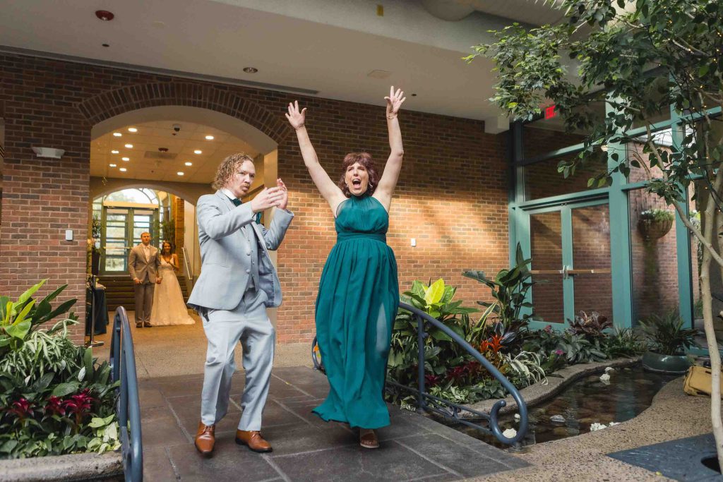 A bride and groom walk out of a building after their wedding ceremony with their hands in the air.