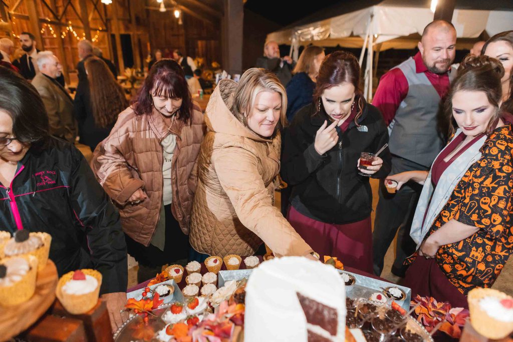A group of people standing around a dessert table at a wedding reception.