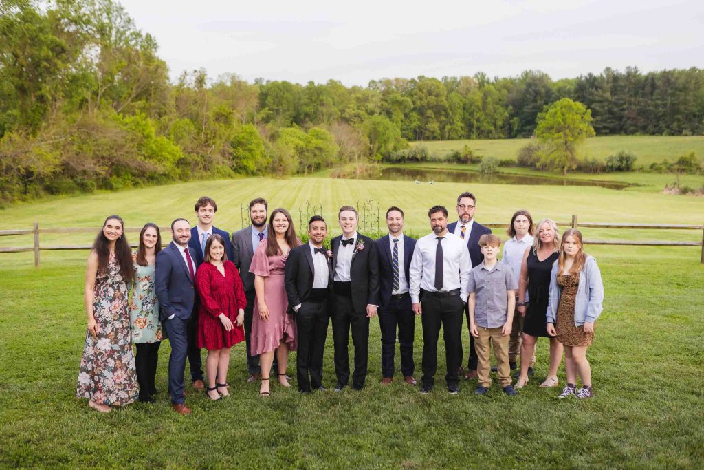 A group of people posing for a wedding portrait in front of a field.