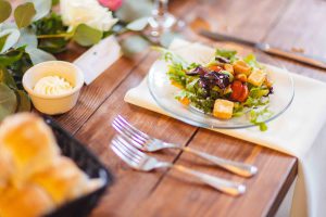 A plate of salad with wedding details on a wooden table.