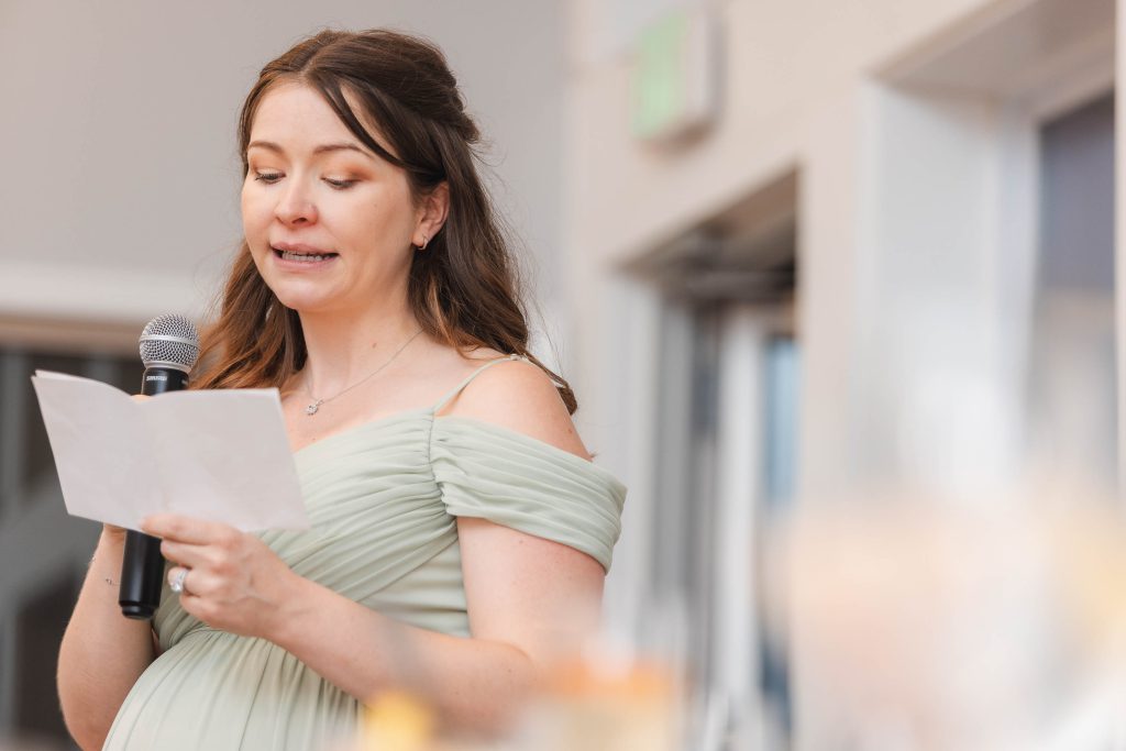 A pregnant woman delivering a speech at a wedding reception.
