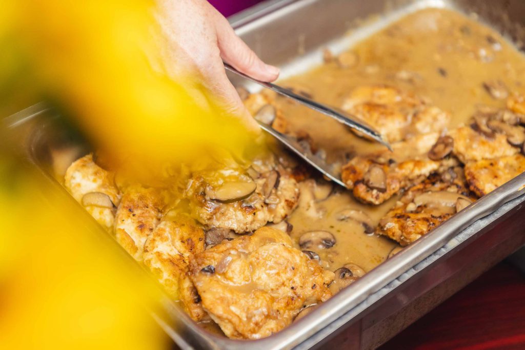 A person pouring gravy over chicken in a pan at a wedding.