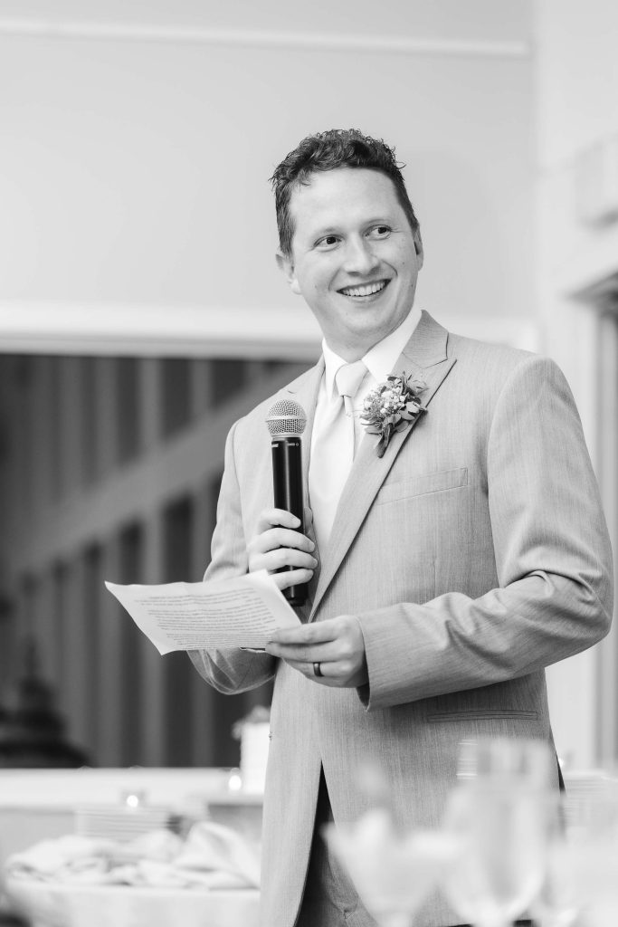 A black and white photo of a groom giving a speech at a wedding reception.