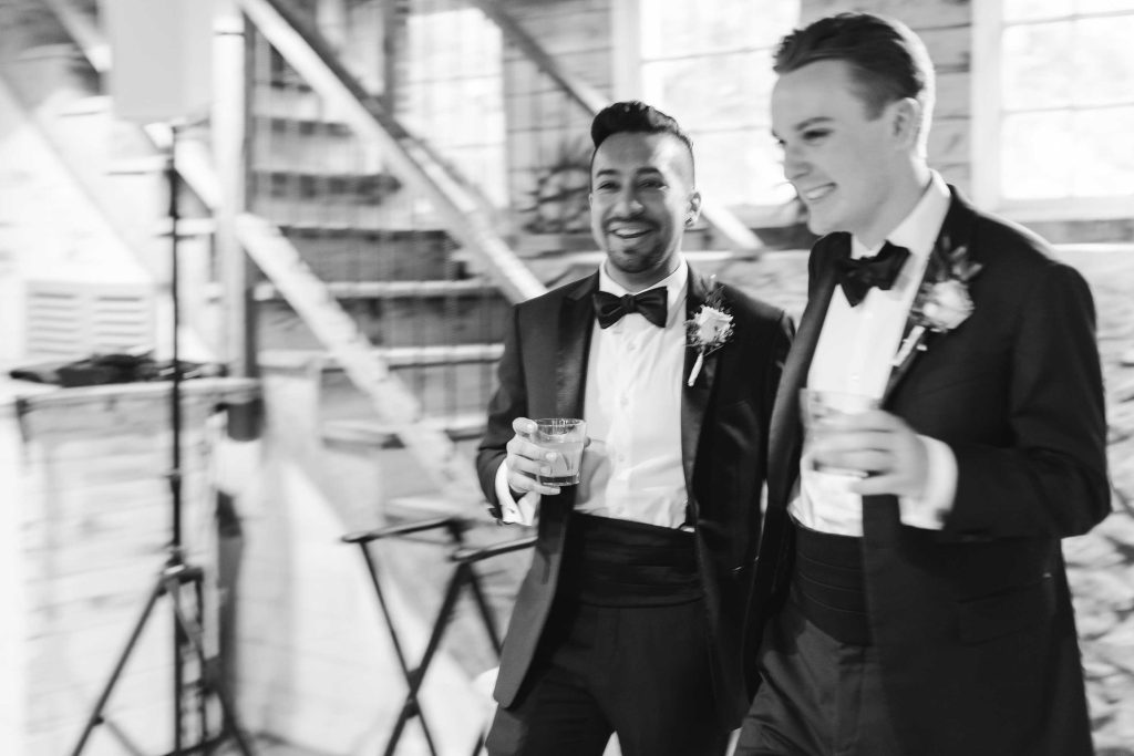 Two groomsmen in tuxedos walking down the aisle at a wedding reception.