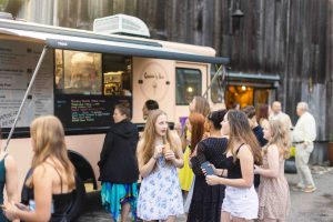 A group of people celebrating a birthday party or quinceanera standing in front of a food truck.