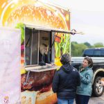 A group of people celebrating a quinceanera in front of a food truck.