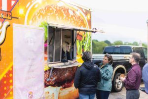 A group of people celebrating a quinceanera in front of a food truck.