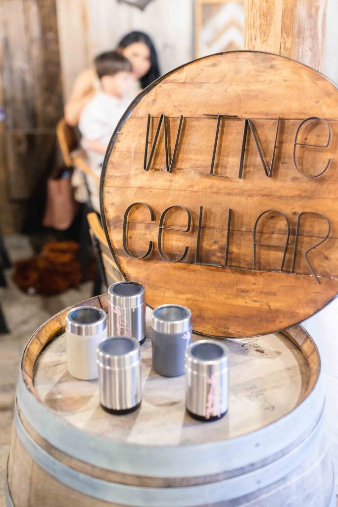 A wooden sign with the words "wine cellar" on it sits on top of a wooden barrel at a birthday party.