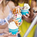 A group of girls celebrating a birthday party with cups of ice cream.