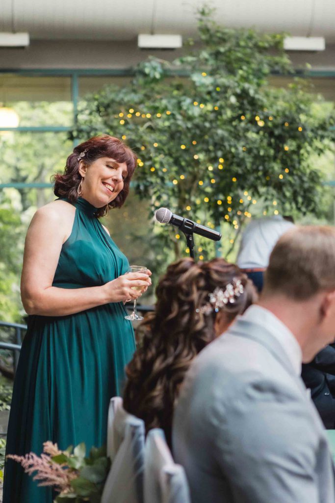 A woman in a green dress is giving a speech at a wedding reception.