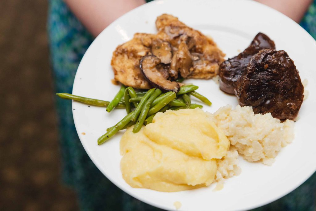 At a wedding reception, a person expertly handles a plate filled with meat, green beans, and mashed potatoes.