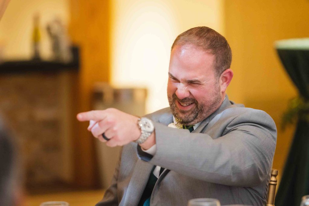 A man in a suit is pointing at a table at a wedding reception.