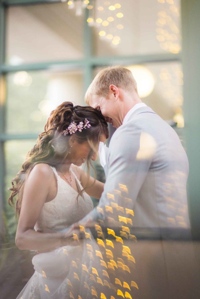 A wedding couple hugging in front of a window at their reception.