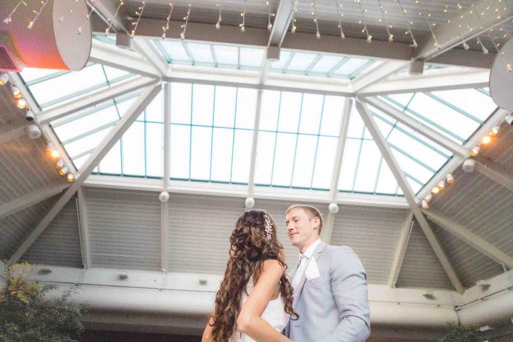 A bride and groom share their first dance at their wedding reception under a skylight.