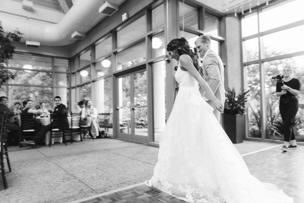 A bride and groom standing in front of a large reception room.