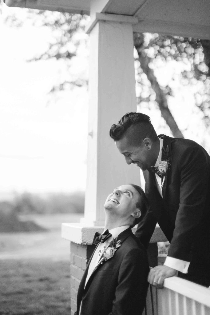 Two men in tuxedos sitting on a porch for a wedding portrait.