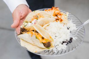 A man showcasing wedding details, holding a plate of tacos and rice.