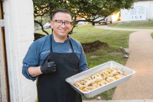 A man holding a tray of food with a thumbs up at a wedding reception.