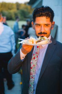 A man with a mustache holding a plate of food at a wedding.