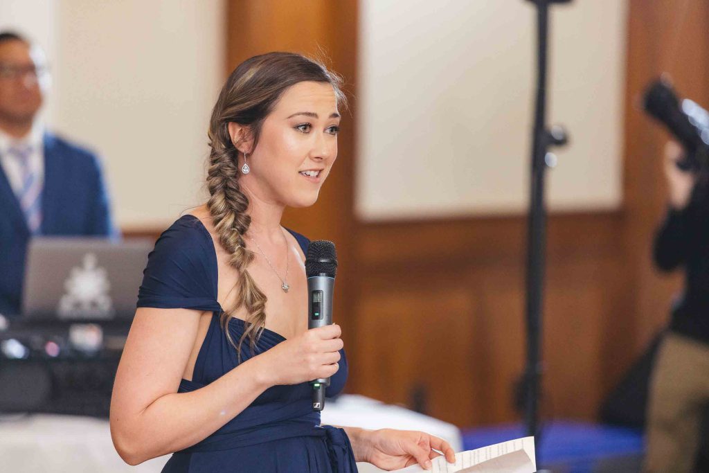 A woman in a blue dress speaking into a microphone at a wedding reception.