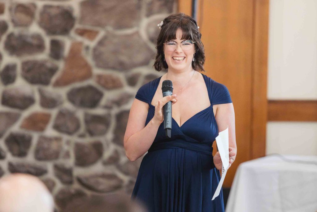 A woman in a blue dress giving a speech at a wedding reception.