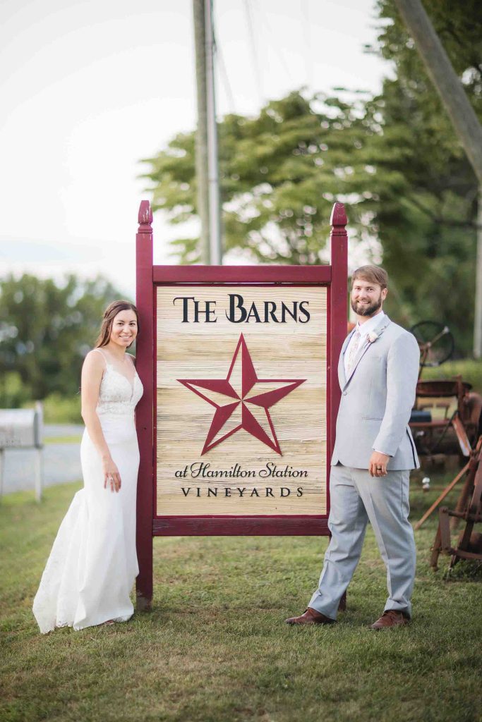 A wedding couple posing in front of a sign at the barns winery.