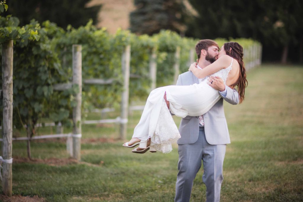 A bride and groom embracing each other in a vineyard for their wedding portrait.