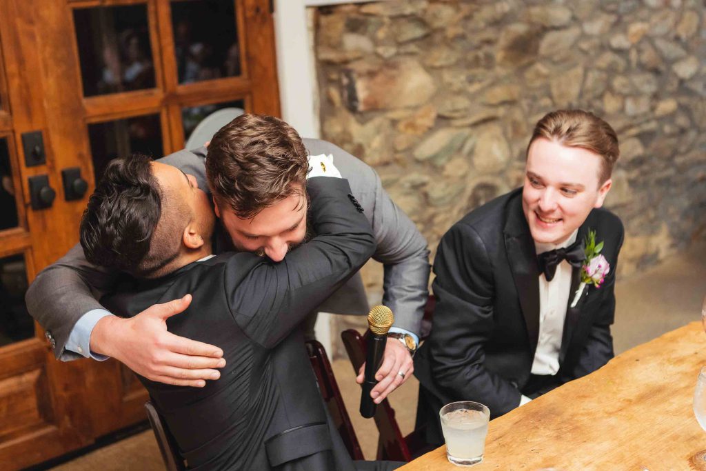 A group of groomsmen hugging each other at a wedding reception.
