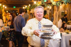 A man holding a cake at a wedding reception, event vendor.