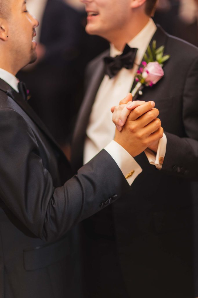 Two men dancing at a wedding reception in tuxedos.