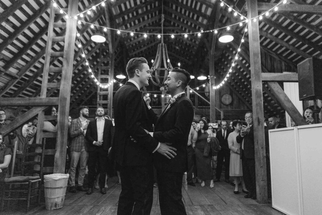 A black and white photo of two men sharing a wedding dance in a barn reception.