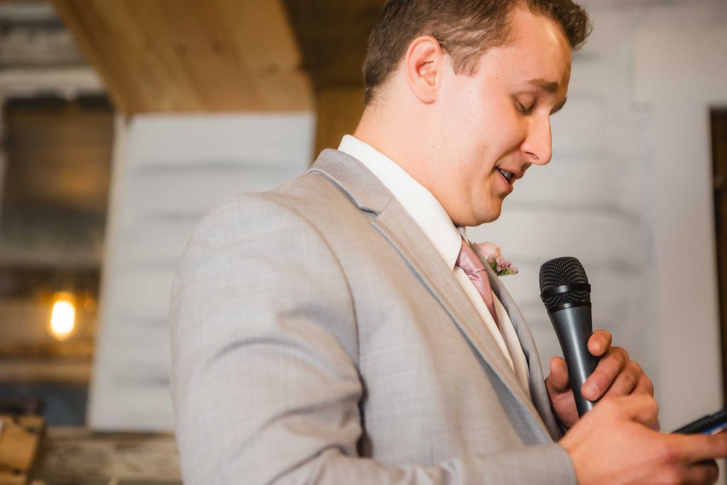 A man in a suit speaking into a microphone at a wedding reception.