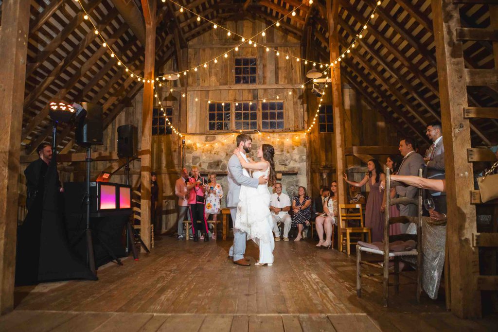 A bride and groom share their first dance at their wedding reception in a barn.