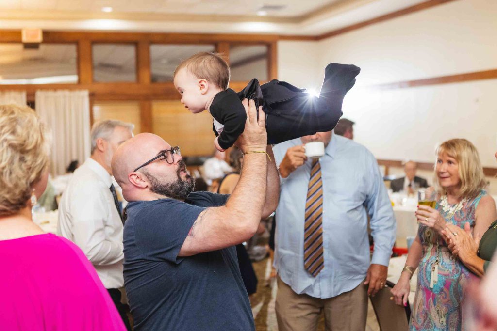A man lifting a baby at a wedding reception.