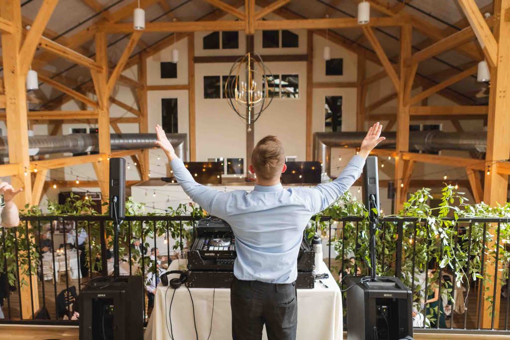 A dj at a wedding reception in a barn with his arms up.