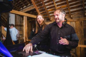 Two men DJing at a barn wedding reception.