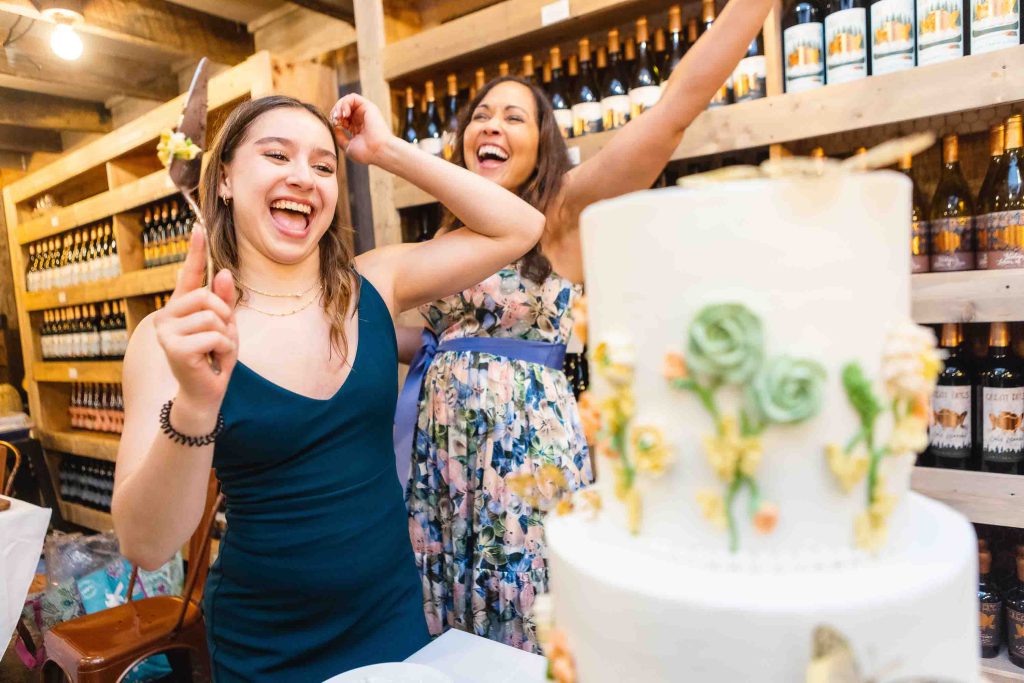 Two women cutting a birthday cake in a wine cellar.
